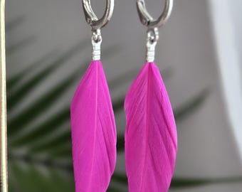 May include: A pair of vibrant hot pink feather earrings featuring silver-toned metal hoop closures. Each earring consists of a single, elongated, bright pink feather attached to a small, circular silver-colored hinged hoop finding.