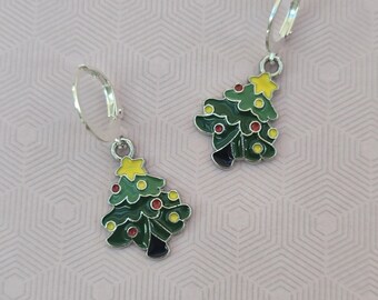 May include: A pair of silver-toned hoop earrings featuring dangling Christmas tree charms. The charms are enameled in green with small yellow star toppers and accented with tiny red and yellow circular ornaments throughout the tree branches.