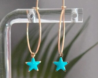 May include: A pair of gold-toned hoop earrings, each featuring a small, bright turquoise star-shaped charm dangling from the bottom. The hoops are thin and circular, with a simple post-back closure mechanism visible at the top of each earring.