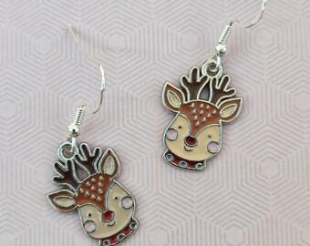 May include: A pair of silver-toned drop earrings featuring enamel reindeer charms. Each charm depicts a reindeer head with brown antlers, a cream-colored face, pink cheeks, a red nose, and a red collar, suspended from silver-toned ear wires.