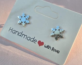 May include: A pair of silver-toned snowflake stud earrings attached to a white display card. The card features the black printed text "Handmade" followed by a red heart icon and the word "with love" in black script lettering.