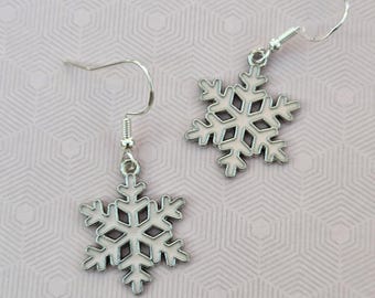 May include: A pair of silver-toned dangle earrings featuring snowflake-shaped charms. Each snowflake has a light pink enamel inlay and is suspended from a simple silver-toned fishhook wire ear wire, creating a delicate and symmetrical winter-themed design.