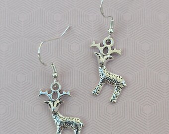 May include: A pair of silver-toned metal earrings featuring a detailed deer or reindeer charm. Each charm is suspended from a simple silver-toned hook wire. The deer design includes textured markings on the body and prominent antlers at the top.