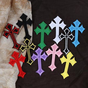 May include: A collection of embroidered cross patches in various colors, including red, black, green, white, blue, pink, purple, and yellow. Each patch features a detailed design with contrasting border stitching, suitable for fabric embellishment.