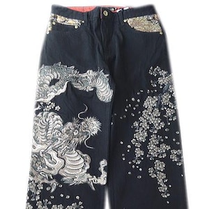 May include: A white ceramic mug with a black handle and the text "But First, Coffee" in a bold, black font. The mug is set against a blurred background, suggesting a cosy setting.