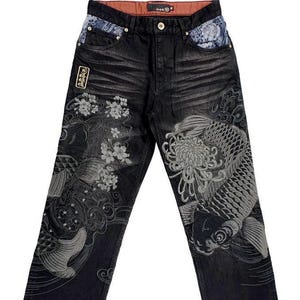 Könnte beinhalten: Schwarze Jeans mit detaillierter Stickerei von Koi-Fischen und Blumenmustern. Die Jeans haben einen Knopfverschluss, Taschen und dekorative Aufnäher. Die Stickerei ist in Grau- und Weißtönen gehalten.