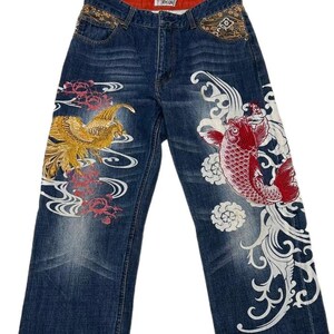 Könnte beinhalten: Dunkelblaue Jeans mit aufwendigen Stickereien. Ein Bein zeigt einen goldenen Phönix, das andere einen roten Koi-Karpfen, mit weißen und rosa Verzierungen. Der Bund hat dekorative Nähte.