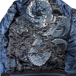 May include: A black satin bomber jacket with a large embroidered dragon design in shades of blue and white. The jacket has blue sleeves and a black and blue striped collar and cuffs. The back of the jacket features a detailed dragon illustration.