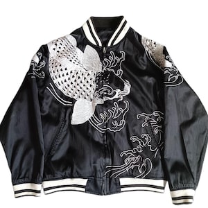 Könnte beinhalten: Eine schwarze Satin-Bomberjacke mit weißer Stickerei von Koi-Fischen und Wellenmustern. Die Jacke verfügt über einen Frontreißverschluss, lange Ärmel sowie gerippte Bündchen an Ärmeln und Saum mit weißen Streifen. Der Kragen ist ebenfalls gerippt.