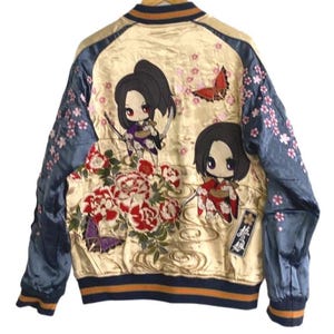 Puede incluir: Una chaqueta bomber de satén color crema con mangas azules y flores de cerezo rosas bordadas. La parte posterior muestra dos personajes estilo anime con espadas, peonías rojas y blancas, una mariposa morada y una roja.