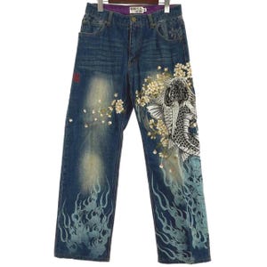 Op de afbeelding: Blauwe denim jeans met een decoratief ontwerp met een koikarper, kersenbloesems en vlamachtige patronen. De jeans hebben een rechte pijp en een knoop- en ritssluiting.