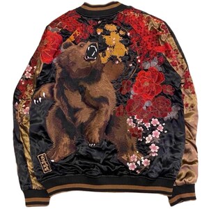 May include: A black satin bomber jacket featuring an intricate back embroidery of a roaring brown bear surrounded by large red peonies and small pink cherry blossoms. The jacket has gold-toned sleeves, a ribbed collar, and a small rectangular patch.