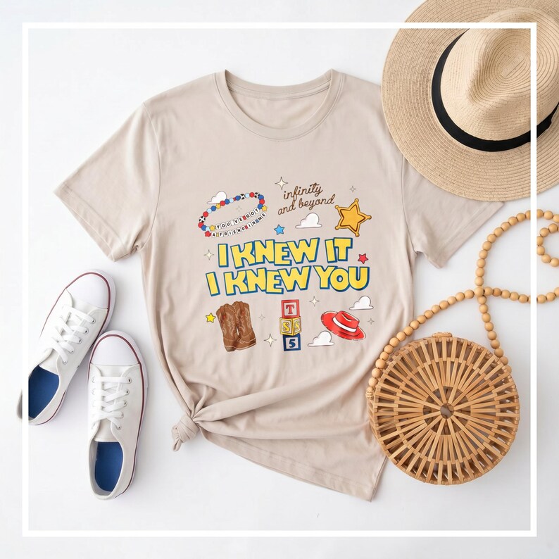 K&ouml;nnte beinhalten: Ein beiges Kurzarm-T-Shirt mit einem Grafikdruck, der den Text I KNEW IT I KNEW YOU, infinity and beyond und You've Got A Friend In Me zeigt. Das Design umfasst ein Perlenarmband, einen gelben Stern, braune Stiefel, Spielw&uuml;rfel und einen roten Hut.
