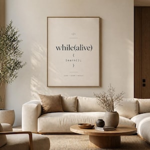 May include: A framed print with the text "while(alive) { learn(); }" in a minimalist style. The print is in a black frame and hangs on a neutral-colored wall. The words "CODE • LEARN • REPEAT" are at the bottom. The print is in a living room setting.