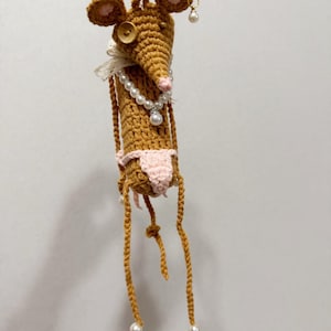 May include: A whimsical, handmade crochet mouse doll with a brown body, pink ears, and a pearl necklace. The mouse wears a pink bikini and has long, dangling legs with pearl accents. A button and lace detail the neck, and pearl earrings complete the look.