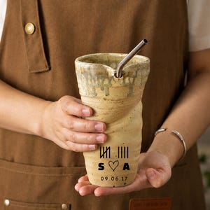 May include: A tall, beige ceramic tumbler with a textured, speckled finish and a metallic straw. The front features black printed tally marks, the letters S and A separated by a heart symbol, and the date 09.06.17 in a simple sans-serif font.