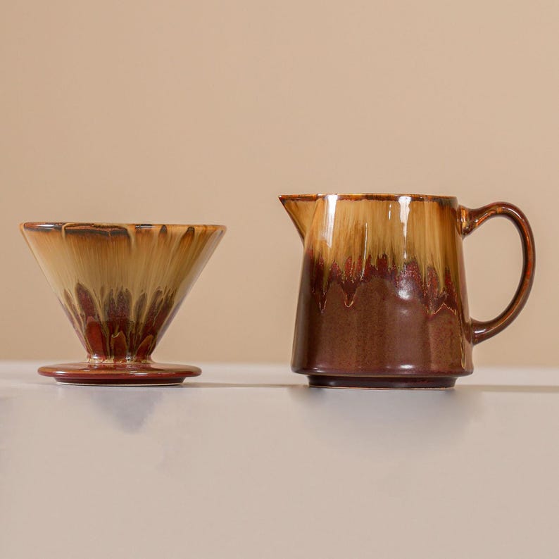 Peut inclure: Un ensemble de cafeti&egrave;re et de pichet en c&eacute;ramique. Le syst&egrave;me de versement a une forme conique avec une base large. Le pichet a une anse et un bec. Les deux pi&egrave;ces ont un gla&ccedil;age marron et beige.