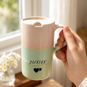 Peut inclure: Un grand mug en céramique au design bicolore pastel, avec une partie supérieure rose pâle et une partie inférieure vert clair. Le mug comprend un couvercle assorti avec une petite ouverture et le nom JACKSON imprimé au-dessus de deux cœurs noirs.