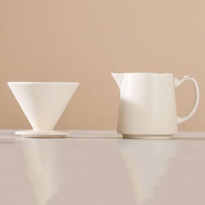 Peut inclure: Un verseur &agrave; caf&eacute; en c&eacute;ramique blanche et une petite cruche assortie avec une poign&eacute;e. Le verseur est en forme de c&ocirc;ne et repose sur une base circulaire. La cruche a un bec et une poign&eacute;e incurv&eacute;e.