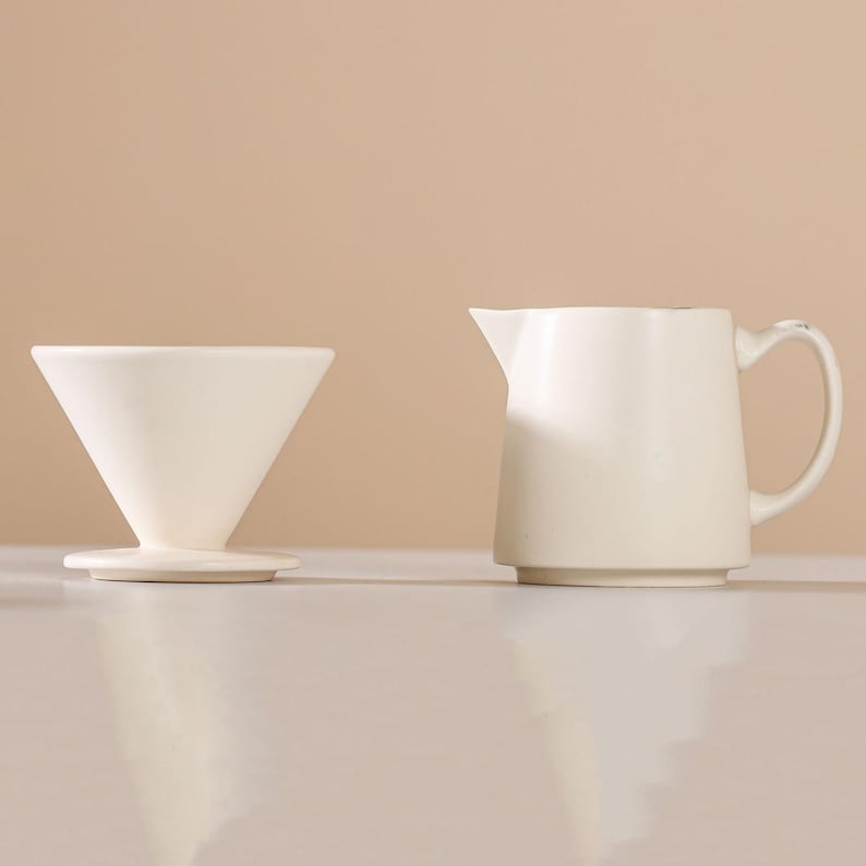 Peut inclure: Un verseur &agrave; caf&eacute; en c&eacute;ramique blanche et une petite cruche assortie avec une poign&eacute;e. Le verseur est en forme de c&ocirc;ne et repose sur une base circulaire. La cruche a un bec et une poign&eacute;e incurv&eacute;e.