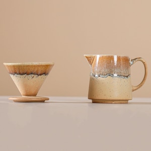 Peut inclure: Un ensemble verseur &agrave; caf&eacute; et pot &agrave; cr&egrave;me en c&eacute;ramique. Le verseur est en forme de c&ocirc;ne avec une base plate. Le pot &agrave; cr&egrave;me a une anse et un bec. Les deux pi&egrave;ces ont une base beige mouchet&eacute;e avec un dessus glac&eacute; marron et blanc.