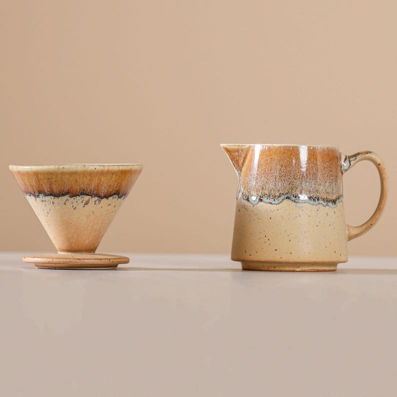 Peut inclure: Un ensemble verseur &agrave; caf&eacute; et pot &agrave; cr&egrave;me en c&eacute;ramique. Le verseur est en forme de c&ocirc;ne avec une base plate. Le pot &agrave; cr&egrave;me a une anse et un bec. Les deux pi&egrave;ces ont une base beige mouchet&eacute;e avec un dessus glac&eacute; marron et blanc.