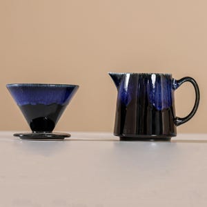 Peut inclure: Un ensemble de cafeti&egrave;re et de pot &agrave; cr&egrave;me en c&eacute;ramique. La cafeti&egrave;re a un int&eacute;rieur &eacute;maill&eacute; bleu fonc&eacute; et un ext&eacute;rieur noir. Le pot &agrave; cr&egrave;me est noir avec un dessus &eacute;maill&eacute; bleu fonc&eacute; et une poign&eacute;e.