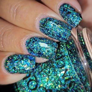 Puede incluir: Primer plano de uñas pintadas con esmalte de uñas brillante azul y turquesa. El esmalte tiene un aspecto texturizado y brillante. El frasco de esmalte de uñas es parcialmente visible, con un frasco de vidrio transparente y una tapa plateada.