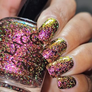 May include: Close-up of a nail polish bottle and painted nails. The nails are covered in a glittery polish with a gradient effect, transitioning from gold to purple. The bottle is filled with a similar glittery polish.