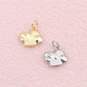 May include: Two small metal charms shaped like chef hats, one finished in a bright gold tone and the other in a polished silver tone. Each charm features a small circular jump ring at the top for attachment, with a smooth, reflective surface.