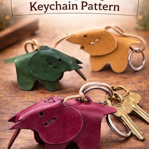 Peut inclure: Trois porte-clés éléphants en cuir vert, beige et bordeaux, avec des anneaux et des clés attachées. Les porte-clés sont sur une surface en bois. Le texte "Leather Toy Elephant Keychain Pattern" est en haut.
