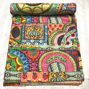 Könnte beinhalten: Eine farbenfrohe, gemusterte Steppdecke mit aufgerolltem Oberteil. Die Steppdecke zeigt ein Patchwork-Design mit Erdbeeren, Blumen und Bögen. Die Farbpalette umfasst Rosa, Blau, Gelb und Grün.