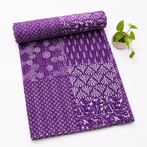 Könnte beinhalten: Eine rechteckige violette Steppdecke mit einem Patchwork-Design aus verschiedenen weißen Blumen-, geometrischen und Blattmustern. Der Stoff weist durchgehend sichtbare weiße Steppnähte auf und der obere Teil ist umgerollt.