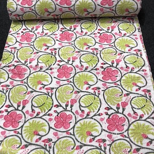 Könnte beinhalten: Eine weiße Steppdecke mit floralem Muster, oben aufgerollt. Das Design umfasst rosa Blüten, grüne Blätter und graue Ranken auf weißem Hintergrund. Die Steppdecke besteht aus einem weichen, gesteppten Stoff.