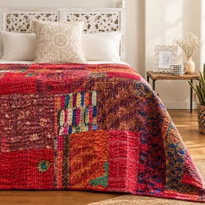 Könnte beinhalten: Eine Patchwork-Tagesdecke mit einer lebendigen Auswahl an roten, rosa, orangefarbenen und blauen Stoffquadraten. Die Decke ist durchgehend mit aufwendigen Kantha-Stichen verziert, die verschiedene florale, geometrische und abstrakte Muster auf der Oberfläche zeigen.