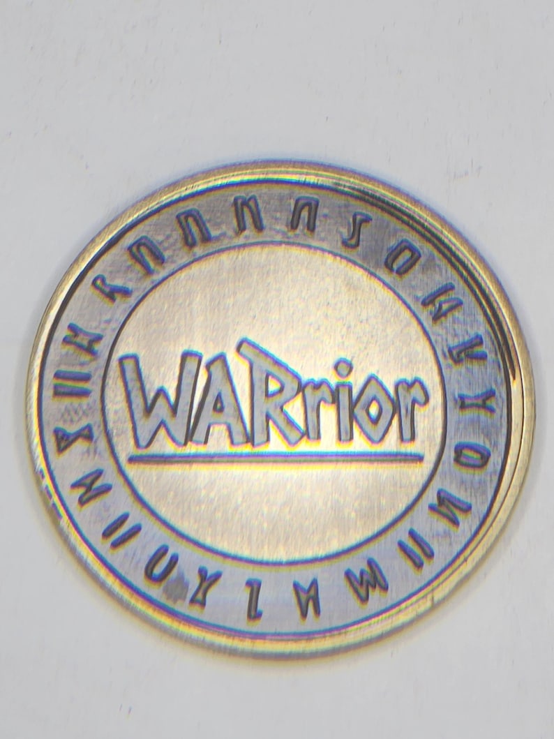 Brass coin engraved with WARrior text, blue tarnish accents and decorative rim, coin engraving files example.