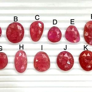 Könnte beinhalten: Elf facettierte Edelsteine in verschiedenen Rot-Tönen, von oval bis unregelmäßig geformt, beschriftet mit Buchstaben A bis K. Die Steine liegen auf einer weißen, geriffelten Oberfläche.