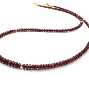 Può includere: Una collana composta da piccole perle rotonde di pietra preziosa rosso scuro disposte in un unico filo. Le perle sono intervallate da minuscoli distanziatori in metallo dorato lucido e il pezzo è rifinito con una chiusura a moschettone dorata.
