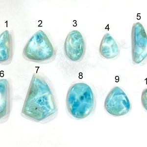 May include: Ten polished larimar gemstones of varying shapes and sizes are displayed against a white background. The stones exhibit a range of blue and white patterns, with some having a marbled appearance. The gemstones are numbered for identification.