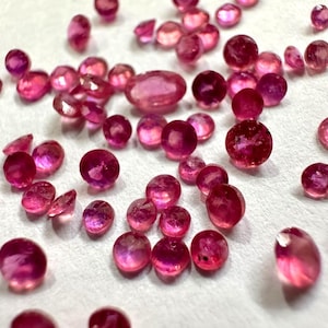 Puede incluir: Una colección de numerosas piedras preciosas pequeñas, sueltas y facetadas en varios tonos de rosa vibrante y rojo intenso. Las piedras son principalmente redondas, con una gema de corte ovalado más grande, todas con superficies reflectantes.