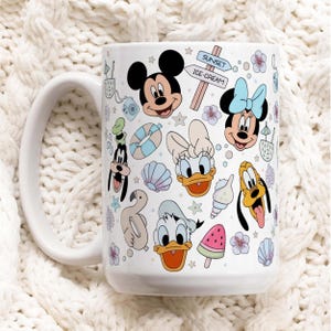 Può includere: Tazza in ceramica bianca con illustrazioni colorate di Topolino, Minnie, Paperino, Paperina, Pippo e Pluto. La tazza presenta anche elementi a tema spiaggia come conchiglie e un fenicottero.