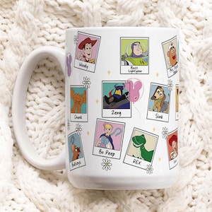 Puede incluir: Taza de cerámica blanca con un asa grande, decorada con retratos de personajes de dibujos animados de la serie de películas Toy Story. La taza presenta imágenes de Woody, Buzz Lightyear y otros personajes en un diseño de marco de fotos.