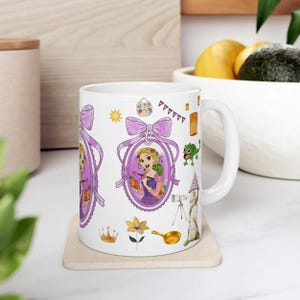 Puede incluir: Taza de cerámica blanca con un retrato enmarcado en púrpura de una princesa de dibujos animados con cabello rubio largo, un camaleón verde y otras ilustraciones temáticas. La taza tiene un asa curva y está decorada con un lazo.
