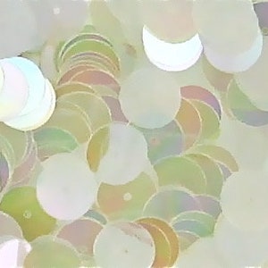May include: A close-up of a container filled with iridescent white and light green sequins. The sequins are various sizes and shapes, including circles and half-circles.