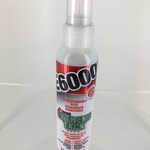 May include: A clear plastic bottle of E6000 Extreme Tack repositionable glue. The bottle is 4 fl oz (118.2 ml) and has a red and white label with the text "E6000 Extreme Tack" and "Create dots of glue. Cree puntos de pegamento."