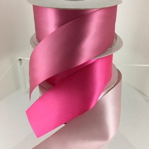 May include: Three spools of satin ribbon in pink, hot pink, and light pink shades. The ribbon is wound around cardboard spools.