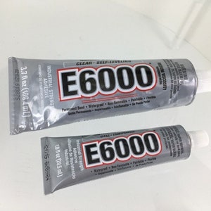 May include: Two tubes of E6000 clear self-leveling adhesive. The larger tube is 3.7 fl oz (109.4 mL) and the smaller tube is 1.0 fl oz (29.5 mL). Both tubes are silver with black text and feature the words "Industrial Strength Adhesive" and "Permanent Bond, Waterproof, Non-flammable, Paintable, Flexible".