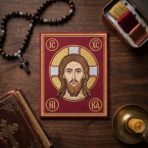 May include: A religious icon patch featuring a detailed embroidered image of Jesus Christ with a halo, set against a burgundy background. The patch is surrounded by gold trim and includes Greek letters. Other items include a rosary, a book, and a candle.