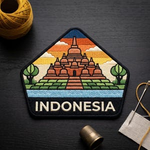 May include: Embroidered patch featuring the Borobudur temple in Indonesia, with a colorful sunset sky and the word "INDONESIA" at the bottom. The patch is surrounded by a black border and includes trees and water elements.
