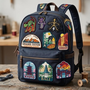 May include: Navy blue backpack adorned with colorful embroidered patches. Patches feature travel destinations like Grand Teton, Kenya, Jordan, Kyoto, and Bali. The backpack has brown leather accents, a top handle, and adjustable straps. The backpack is sitting on a wooden surface.